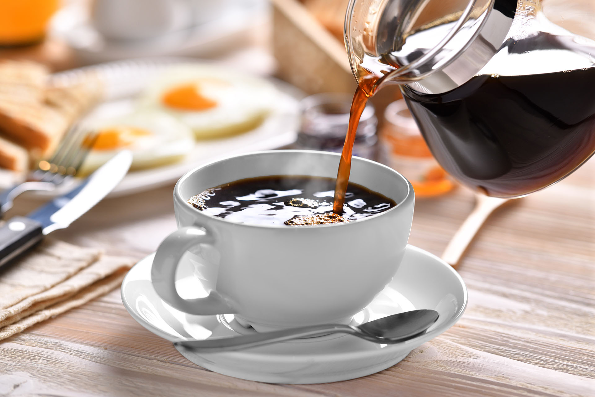 Pouring coffee on a cup with breakfast on wooden table